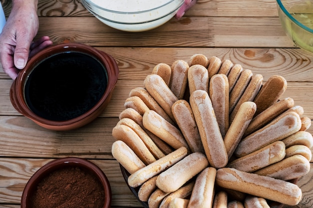 Zutaten für ein hausgemachtes Tiramisu. Spezieller Käsekuchen mit Zucker, Eiern, Kaffee, Kakao und Keksen. Rustikaler Holzhintergrund