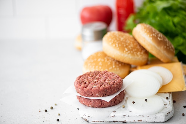 Zutaten für einen Hamburger - Fleischkotelett, Brötchen, Käse, Gemüse auf einem weißen Brett