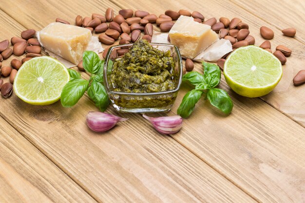 Zutaten für hausgemachtes Pesto: Basilikumblätter, Parmesan, Pinienkerne, Knoblauch, halbe Zitrone. Draufsicht. Heller Holzhintergrund. Speicherplatz kopieren