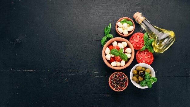 Zutaten für italienischen Caprese-Salat Mozzarella-Käse Kirschtomaten Basilikumblätter Oliven Öl Pfeffer auf schwarzem Hintergrund aus Holz Freier Platz für Text