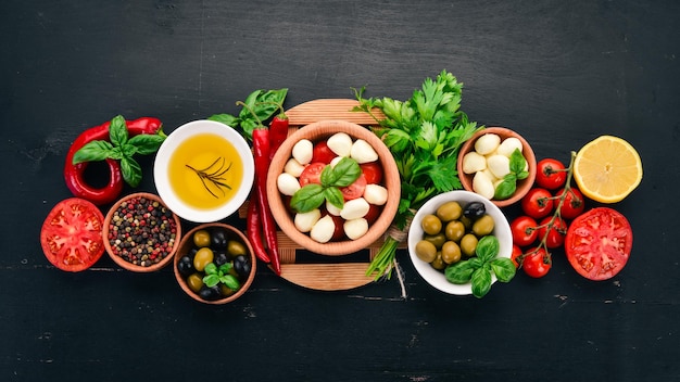 Zutaten für italienischen Caprese-Salat Mozzarella-Käse Kirschtomaten Basilikumblätter Oliven Öl Pfeffer auf schwarzem Hintergrund aus Holz Freier Platz für Text