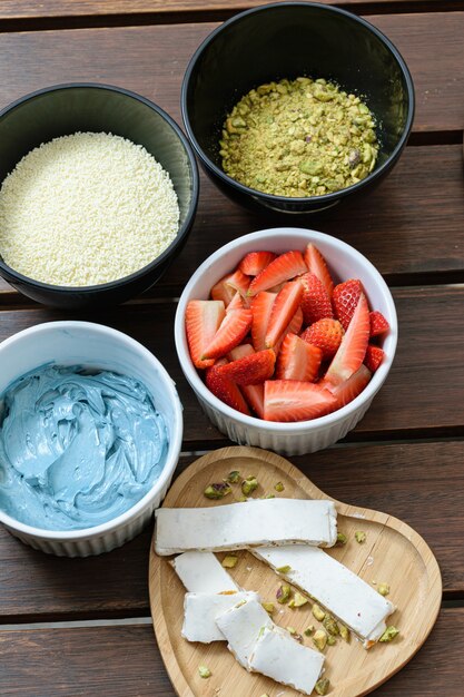 Zutaten für Kuchen, Erdbeeren, blaue Buttercreme, weiße Schokoladenstreusel und gehackte Pistazien. Neben Turron.