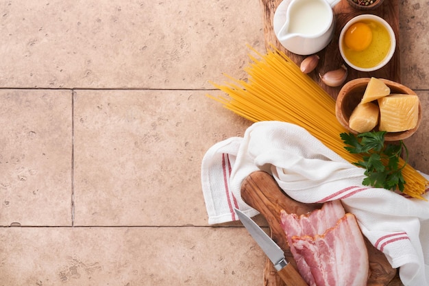 Zutaten für Pasta Carbonara Traditionelle italienische Pasta Carbonara Zutaten Speck Spaghetti Parmesan und Eigelb Knoblauch Beige alte Kachel Tisch Hintergrund Ansicht von oben Kopieren Sie Platz