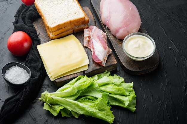 Zutaten für Sandwich, Speck, Käse, Tomaten, Hühnerfleisch, Salat, Sauce, auf schwarzem Tisch