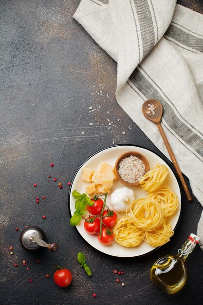 Zutaten für traditionelles italienisches Nudelgericht. Ungekochte rohe Tagliatelle Bolognesi, Parmesan, Olivenöl, Knoblauch, Basilikumblätter, Pfeffer, Kirschtomaten. Draufsicht