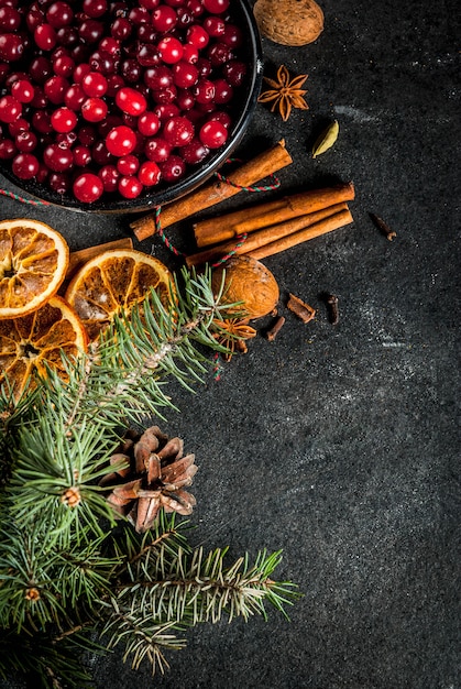 Zutaten für Weihnachten, Winterplätzchen backen. Lebkuchen, Obstkuchen, saisonale Getränke. Moosbeeren, getrocknete Orangen, Zimt, Gewürze auf einer schwarzen Steintabelle, Kopienraum