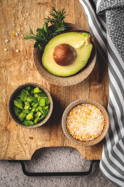 Zutaten und Gewürze zum Kochen auf einem Holzbrett: Avocado, Kräuter, Zwiebeln, Salz, Draufsicht