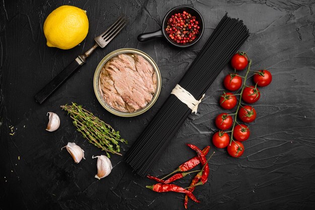 Zutaten ungekochte Nudeln mit Thunfisch und Tomaten, auf schwarzem, dunklem Steintischhintergrund, Draufsicht flach