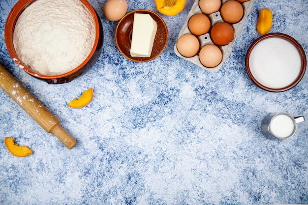 Zutaten zum Backen - Eier, Mehl, Zucker, Butter, Milch auf hellblauem Beton-, Stein- oder Schieferhintergrund. Draufsicht mit Platz für Text.