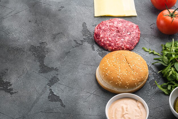 Zutaten zum Kochen von Burgern. Hackfleischpastetchen, Brötchen, Tomaten, Kräuter und Gewürze, auf grauem Steintisch