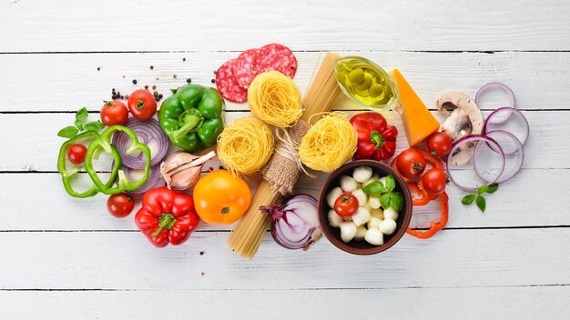 Zutaten zum Kochen von Nudeln Trockene Nudeln Pilze Würstchen Tomaten Gemüse Draufsicht auf weißem Holzhintergrund Freier Kopierplatz