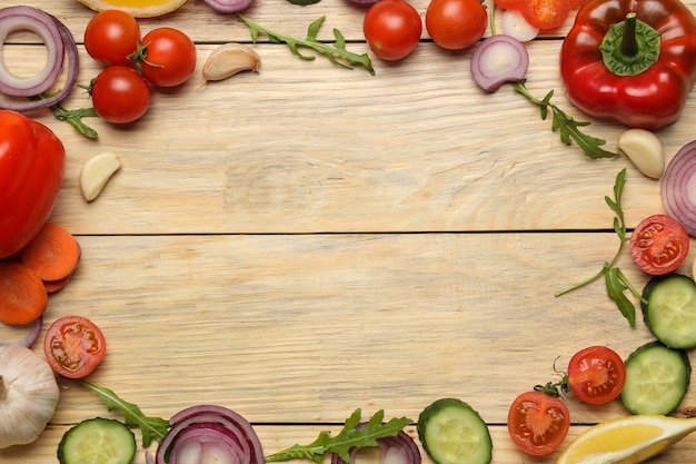 Zutaten zum Kochen von Salat. Rahmen aus verschiedenen Gemüse und Gewürzen Karotte, Tomate, Zwiebel, Gurke, Pfeffer und Rucola auf einem natürlichen Holztisch. Ansicht von oben.