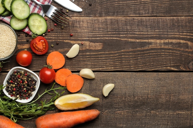 Zutaten zum Kochen von Salat. Verschiedene Gemüse und Gewürze Karotten, Tomaten, Gurken, Paprika und Rucola auf einem braunen Holztisch. Ansicht von oben.