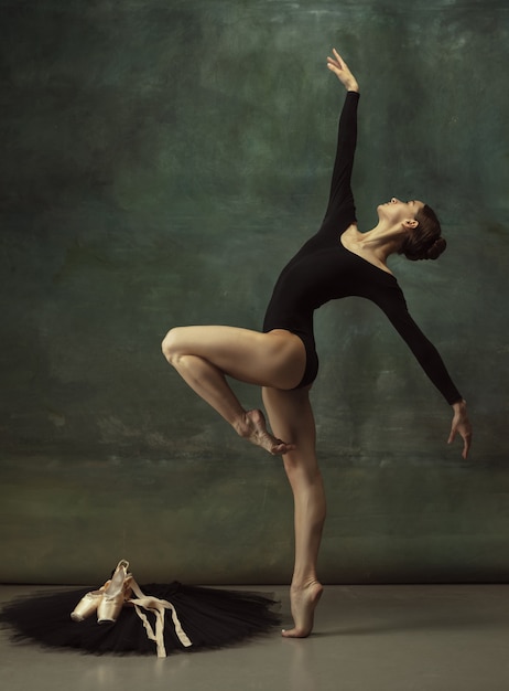 Zuversichtlich. Anmutiger klassischer Ballerinatanz, posiert einzeln auf dunklem Studiohintergrund. Eleganz schwarzes Tutu. Anmut, Bewegung, Aktion und Bewegungskonzept. Sieht schwerelos aus, flexibel. Modisch.