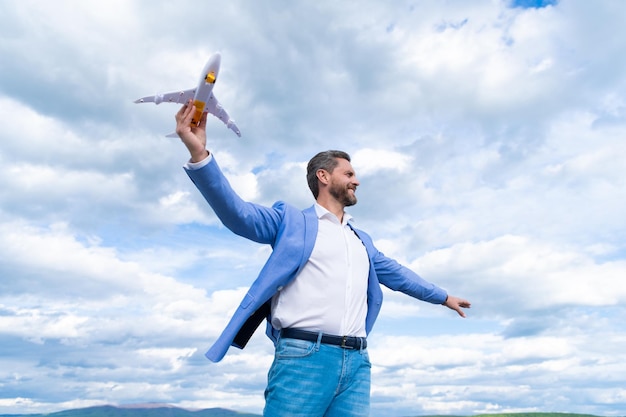 Foto zuversichtlich glücklicher geschäftsmann in jacke halten spielzeugflugzeug auf himmelshintergrund, geschäftserfolg