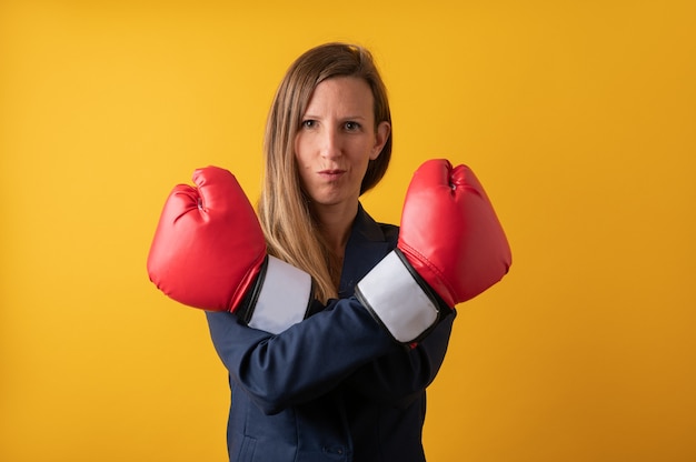 Zuversichtlich junge Geschäftsfrau, die ihre Hände mit roten Boxhandschuhen kreuzt. Über gelbem Hintergrund.