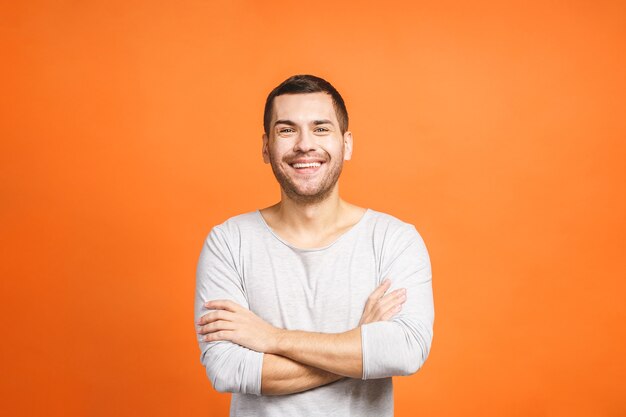 Foto zuversichtlich junger schöner mann, der arme verschränkt hält und lächelt, während er gegen orange hintergrund steht