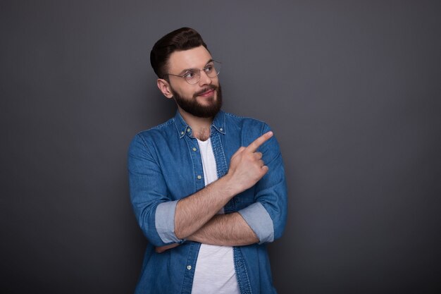 Zuversichtlich kluger moderner bärtiger Mann in lässiger Jeanskleidung und Brille posiert