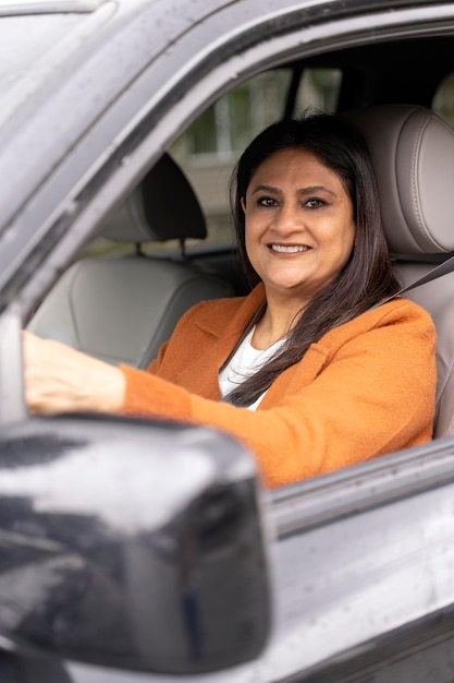 Zuversichtlich lächelnde reife indische Frau, die ein neues Auto fährt und in die Kamera schaut Transport