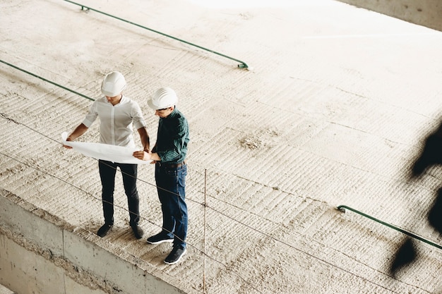 Zuversichtlich Meister gekleidet in weißem Hemd, der den Plan des Gebäudes betrachtet und mit dem Architekten über die Arbeit innerhalb des Gebäudes im Bau spricht.