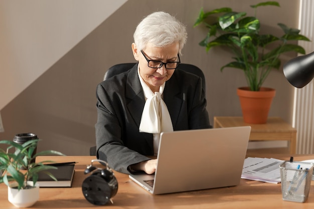 Zuversichtlich stilvolle europäische Seniorin mittleren Alters mit Laptop am Arbeitsplatz stilvolle ältere reife s