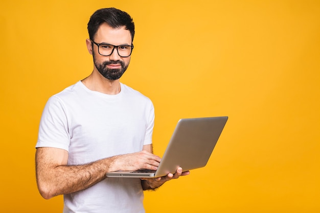 Zuversichtlicher Geschäftsexperte. Zuversichtlich junger gutaussehender bärtiger Mann in lässigem Halten des Laptops und lächelnd, während über lokalisiertem gelbem Hintergrund stehen.