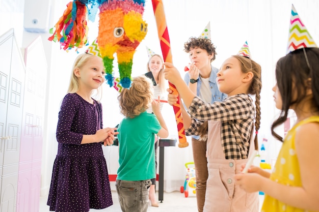 Zuversichtliches Mädchen, das bunte Pinata an der Kinderfeier schlägt