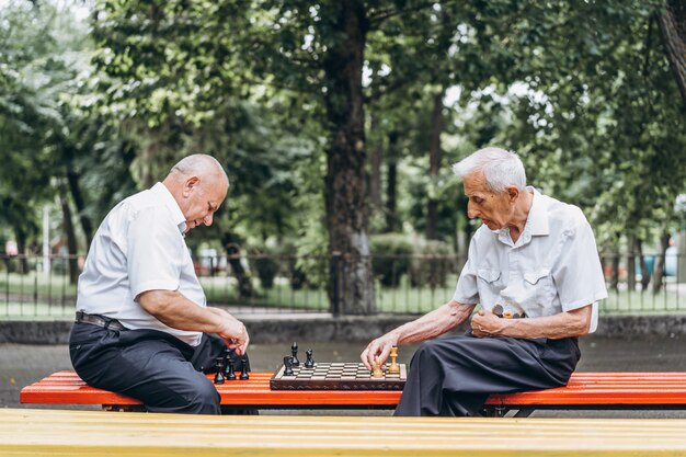 Zwei ältere erwachsene Männer, die Schach auf der Bank draußen im Park spielen.