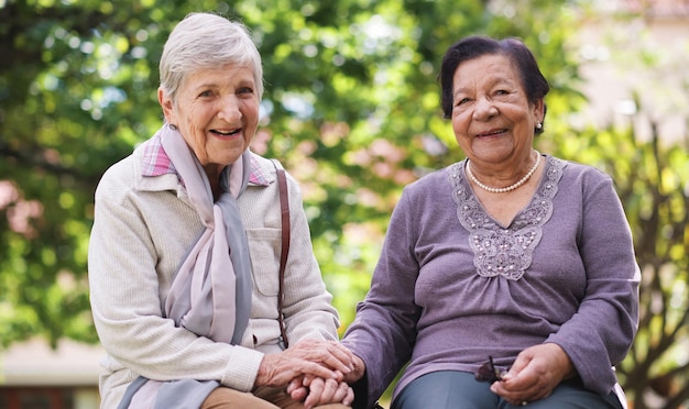 Foto zwei ältere frauen, die auf einer bank im park sitzen und sich an den händen halten, lächeln glückliche lebenslange freunde, die den ruhestand genießen