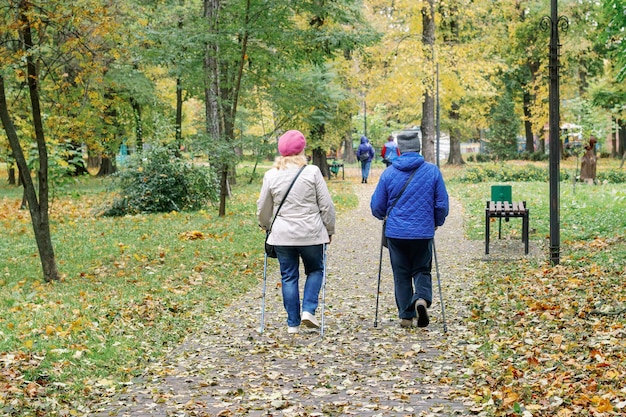 Foto zwei ältere frauen gehen im park und unter den bäumen nordisch spazieren.