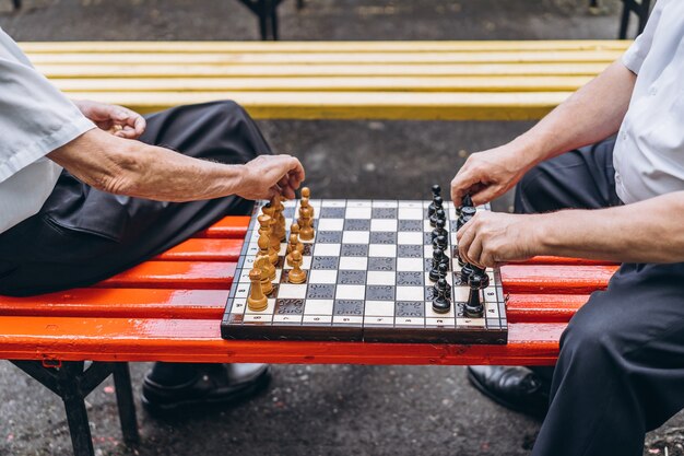 Zwei ältere Männer, die Schach auf der Bank draußen im Park spielen