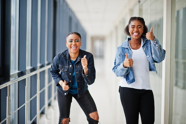 Zwei afrikanische Freundinnen in Jeansjacke zeigen zusammen den Daumen nach oben.