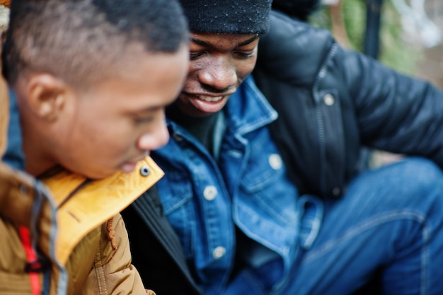 Zwei afrikanische männliche Freunde sitzen und schauen zusammen am Telefon