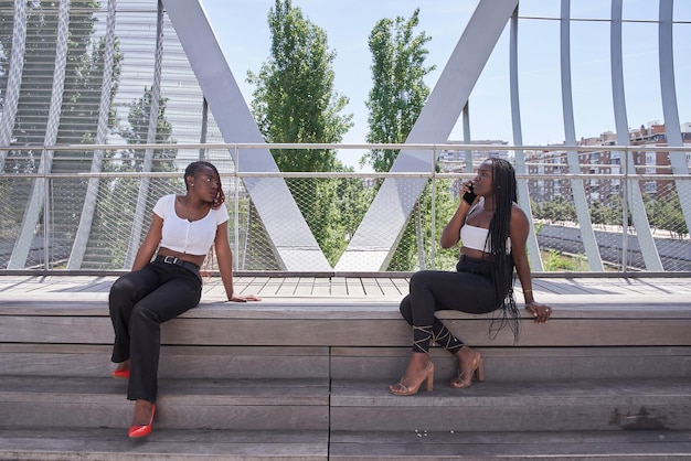 Zwei afroamerikanische Frauen sitzen in einem Park und unterhalten sich über ein Mobiltelefon