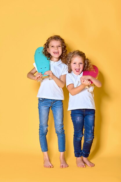 Zwei aktive und glückliche Mädchen mit lockigem Haar, die Spaß mit Penny Board haben, lächelndes Gesicht stehen Skateboard