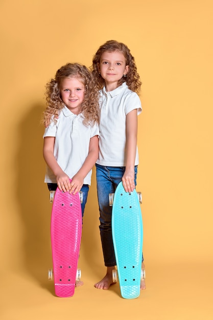 Zwei aktive und glückliche Mädchen mit lockigem Haar, die Spaß mit Penny Board haben,