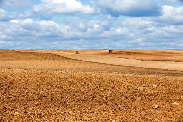 Zwei alte Traktoren pflügen den Boden auf dem Feld, während sie das Feld für die Aussaat vorbereiten, Landschaft in der wolkigen Tageszeit