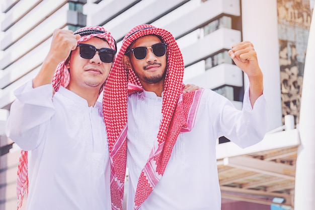 Zwei arabische Geschäftsmänner, die stehen, indem sie beide Hände in der Stadt anheben