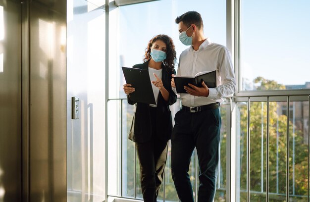 Zwei Arbeiter in Schutzmasken diskutieren Projektarbeit im Büro während der Quarantäne