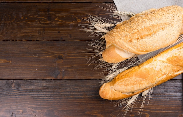 Zwei Arten von Baguette-Broten mit Schlitzen oben und Sesam zwischen Vollkornstielen über einem dunkelbraunen Tisch