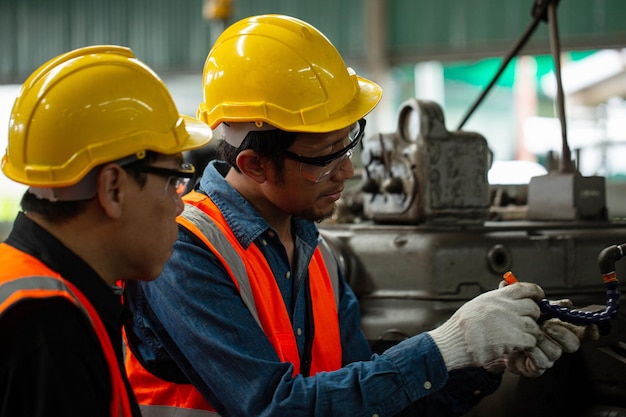 Zwei asiatische Arbeiter prüfen die Statusaufgabe in der Produktionslinie.Arbeitsplatzbetrieb.Zwei Ingenieure an der seitlichen Wartungsmaschine.