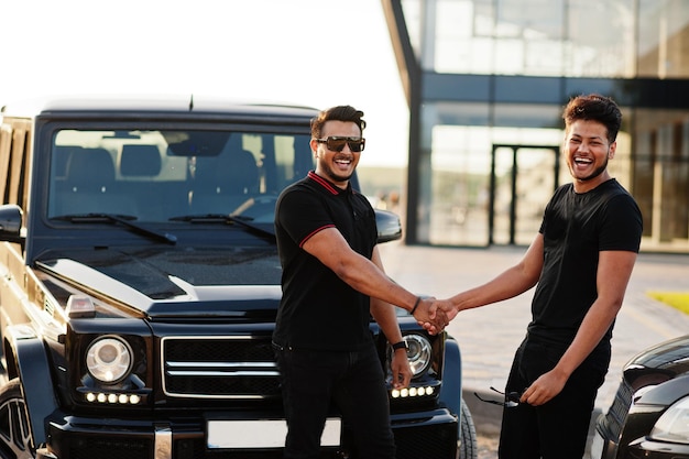 Zwei asiatische brüder tragen ganz schwarz in der nähe von suv-autos und handschütteln.