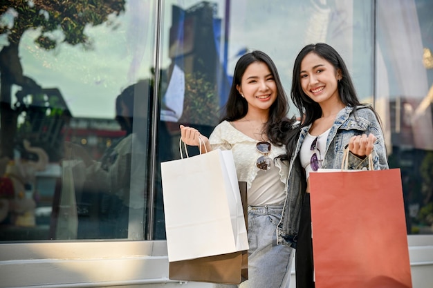 Zwei asiatische Frauen, die lächelnd in die Kamera schauen und ihre Einkaufstaschen tragen