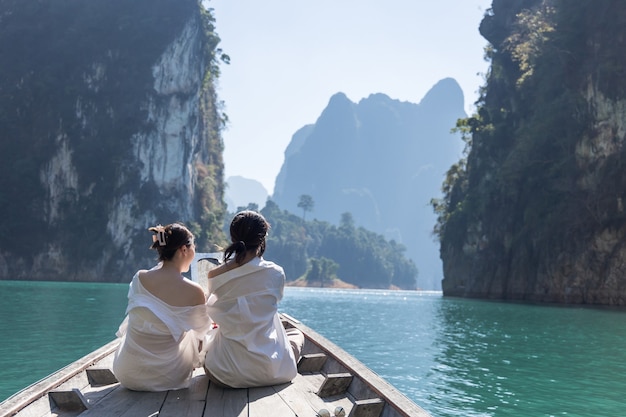 Zwei asiatische Frauen in weißen Hemden sitzen während einer Reise in Thailand vor einem Boot mit einem wunderschönen Berg mitten im Meer. Schönes Thailand.