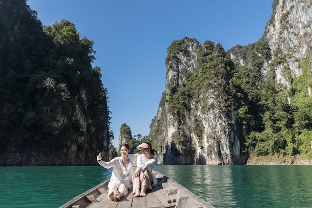 Zwei asiatische Frauen in weißen Hemden sitzen während einer Reise in Thailand vor einem Boot mit einem wunderschönen Berg mitten im Meer. Schönes Thailand.