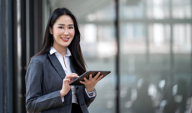 Zwei asiatische Geschäftsfrauen arbeiten gemeinsam an einem digitalen Tablet. Kreative weibliche Führungskräfte treffen sich lächelnd in einem Büro mit einem Tablet-PC