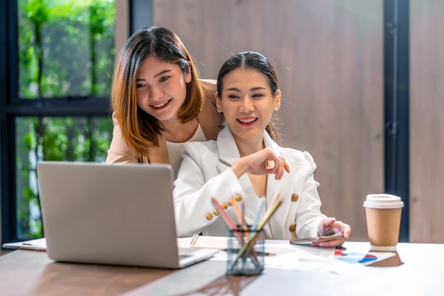 Zwei asiatische geschäftsfrauen, die mit dem partnergeschäft über technologielaptop im modernen konferenzzimmer-, büro- oder arbeitsraum-, kaffeepausen-, partner- und kollegekonzept arbeiten