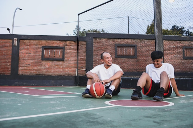 Zwei asiatische junge Freunde entspannen und unterhalten sich nach dem Spiel auf dem Basketballplatz