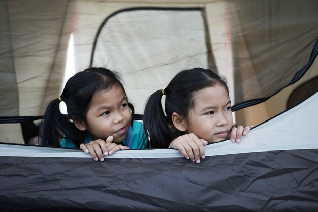 Zwei asiatische Kinder, die sich hinlegen und zusammen im Zelt auf dem Campingplatz spielen, während sie mit der Familie campen