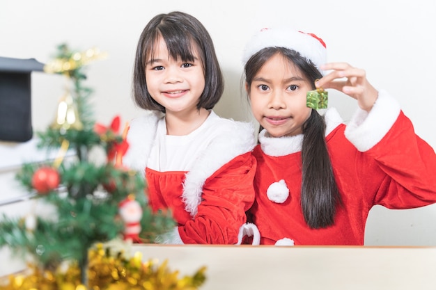 Zwei asiatische Kinder kleine Mädchen tragen Weihnachtsweihnachtsmann, der den Weihnachtsbaum schmückt. Weihnachtsferienkonzept Stockfotos